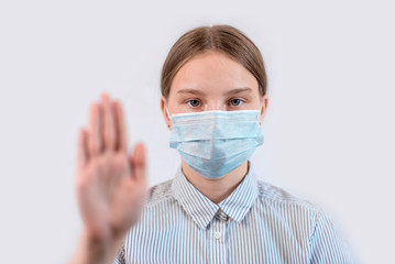 Teenager girl 12-15 years old, in a medical mask covers her face, stop hand gesture, attention is dangerous, white background, COVID-19 sars-cov-2 epidemic pandemic virus outbreak protection concept.