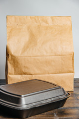 A brown craft paper bag and a black container for taking out or delivering goods and food on a wooden table. Place for advertising. delivery service concept - 345190477