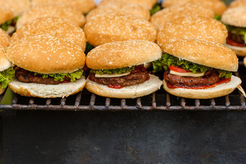 A lot of burgers lie on the grill. Catering food preparation for outdoor party. Barbeque for big company