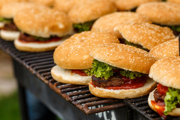 A lot of burgers lie on the grill. Catering food preparation for outdoor party. Barbeque for big company