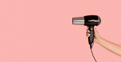 Unrecognizable girl showing hairdryer on pink background, empty space. Panorama - obrazy, fototapety, plakaty