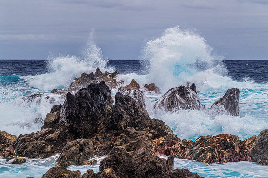 Ocean waves break against coastal cliffs on a cloudy summer day