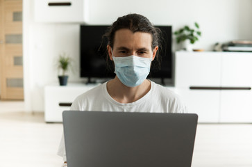 Man in medical mask is working from home with a laptop because of coronavirus epidemic. Remote work during pandemic. Stay home during COVID-19 quarantine concept. Freelancer.