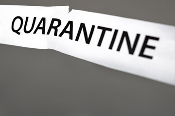 End of a coronavirus quarantine concept. Torn paper with the word Quarantine. Pandemic of COVID-19 is over. Finish of isolaion. Close up. Grey background. Release from Quarantine