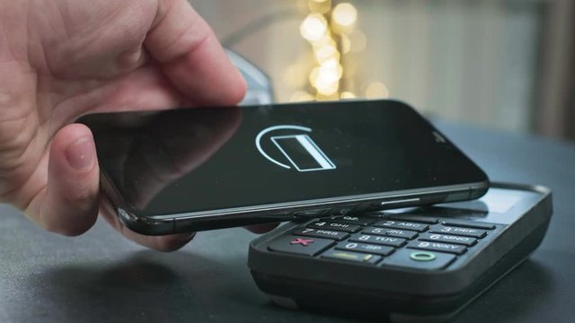 Pay by phone on the POS contactless payment terminal. A user makes a purchase using a smartphone in a store or restaurant. E-money at cashless wallet.