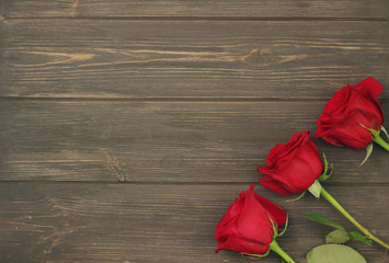 Fototapeta na wymiar Three beauty red roses with green leaves on the right on wooden background with space for text. Romantic gift