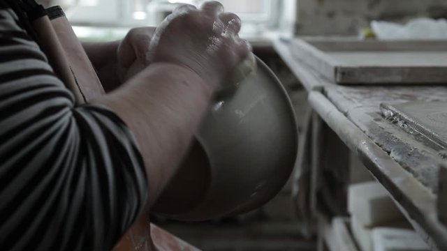 Clay workshop. Full of feminine hands holding a wet rag. Remove the roughness on the clay pot. Close up. Grayscale.