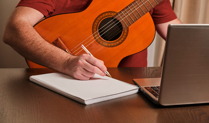 man playing guitar at home. Online course. Studying with a notebook , a laptop and a pen.