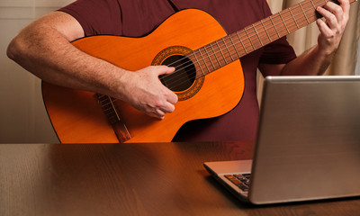man playing guitar at home. Online course. Studying with a laptop.