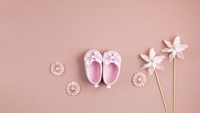 Cute newborn baby girl shoes with festive decoration over pink background. Baby shower, birthday, invitation or greeting card idea. Stop motion animation