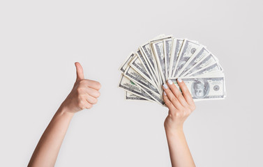 Wealthy woman with money showing thumb up gesture on light background, close up