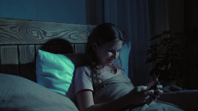 Youth addiction. Igeneration lifestyle. Teen girl surfing Internet on smartphone in bed at night.