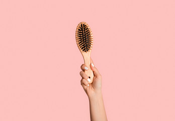 Closeup of millennial girl holding wooden hairbrush on pink background