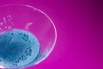 blue liquid in a cocktail martini glass on a pink background