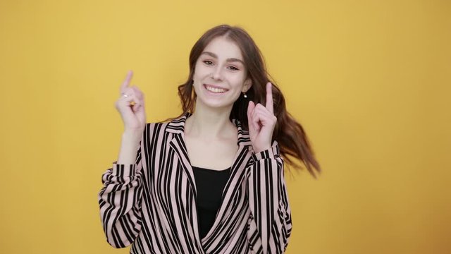 Cute Young Woman Light Brown In Striped Pink And Black Shirt On A Yellow Background, A Happy Girl Smiles And Holds Up Her Index Finger As Sign Of New Thought