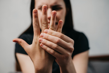 Close up of unhappy tired young woman sitting on bed massaging hand suffering from rheumatoid...