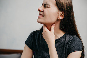 Cropped portrait of sick tired unhappy young woman sitting on bed at home feeling bad suffering from throat pain, painful swallowing, Health Concept.