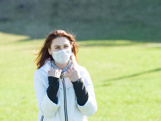 Beautiful young woman in a medical mask on nature in spring afternoon. Coronavirus pandemic