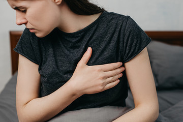 Cropped portrait of sad worried girl suffers from heartache sitting on bed at home, upset young...