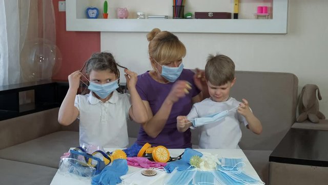 Mother teaches children to wear medical masks indoors. Social distancing and self-isolation in quarantine during the COVID-19 pandemic.