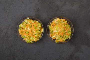 Fresh cabbage salad with carrots in a bowl on a dark gray background top view