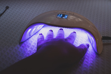 Woman includes lamp and dries her nails with shellac in UV lamp. Close-up.