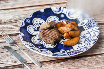 Grilled steak with baked golden potatoes on a wooden background. Top view. Delicious Recipe. Pork Fillet Cooked on Skillet for Dinner . Fried Juicy Meat Texture. Horizontal photo.