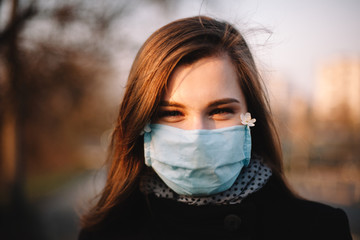 Portrait of happy teenage girl wearing protective face medical mask standing outdoors on city street during spring