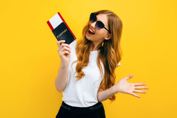 beautiful woman with dark glasses holding a passport and tickets on a yellow background. The concept of travel, business