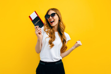 beautiful woman with dark glasses holding a passport and tickets on a yellow background. The concept of travel, business