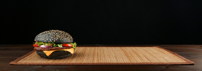 black burger on bamboo mat on black background with copy space