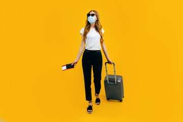 A female passenger in a medical protective mask on her face, with a suitcase and passport, goes abroad. Concept of travel, quarantine and coronavirus
