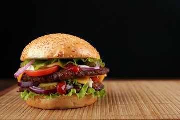 fresh homemade burger close up with copy space. double cheeseburger on bamboo mat on black background. 