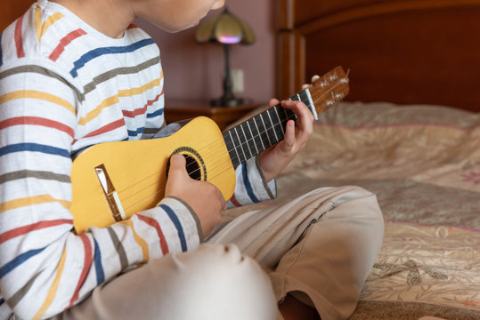 Side view of a little boy playing timple at home.