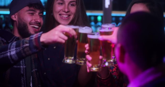 Multi-ethnic group of friends toasting and drinking beer inside bar