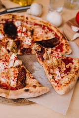 Slice of fresh homemade pizza with sun-dried tomatoes, chicken, cheese and chili peppers on wooden background. Mashrooms, tomato, spice and knife.