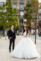 Naklejka premium Bride and groom dancing in the old town street. Wedding couple walks in Budapest near Parliament House. Caucasian happy romantic young couple celebrating their marriage. Wedding and love concept.