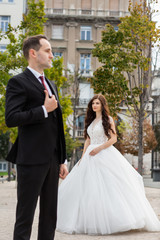 Fototapeta premium Bride and groom dancing in the old town street. Wedding couple walks in Budapest near Parliament House. Caucasian happy romantic young couple celebrating their marriage. Wedding and love concept.