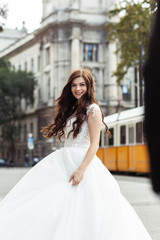 Fototapeta premium Bride in the old town street. Wedding walks in Budapest near Parliament House. Caucasian happy romantic young woman celebrating her marriage. Wedding and love concept.