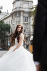 Fototapeta premium Bride in the old town street. Wedding walks in Budapest near Parliament House. Caucasian happy romantic young woman celebrating her marriage. Wedding and love concept.