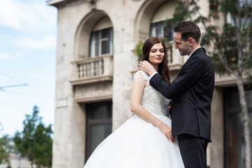 Bride and groom hugging in the old town street. Wedding couple walks in Budapest near Parliament House. Caucasian happy romantic young couple celebrating their marriage. Wedding and love concept.