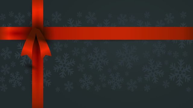 rectangular gift covered with dark christmas wrapping paper with soft snowflakes and a long red bow on the upper left corner