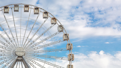 ferris wheel for family holidays with cabs design of white color against the sky with clouds and nobody, side view copy space.