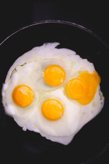 Fried eggs in frying pan. Four eggs. Making breakfast for family. Family weekend breakfast. Quick easy brunch breakfast. Over medium fried eggs. Egg yolk, egg whites. Black stove top. Broken egg yolk