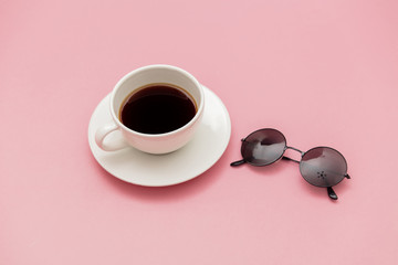 Obraz na płótnie Canvas Cup of coffee and sunglasses on pink color table