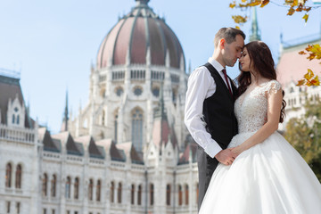 Bride and groom hugging in the old town street. Wedding couple walks in Budapest near Parliament House. Caucasian happy romantic young couple celebrating their marriage. Wedding and love concept.