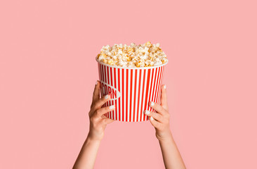 Young girl holding striped bucket with popcorn on pink background, closeup view