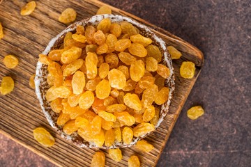 Organic dried golden raisins in ceramic plate on wooden board. Brown background, top view