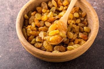 Organic dried golden raisins in wooden bowl.Brown background, close up.