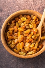 Organic dried golden raisins in wooden bowl.Brown background, vertical format, top view